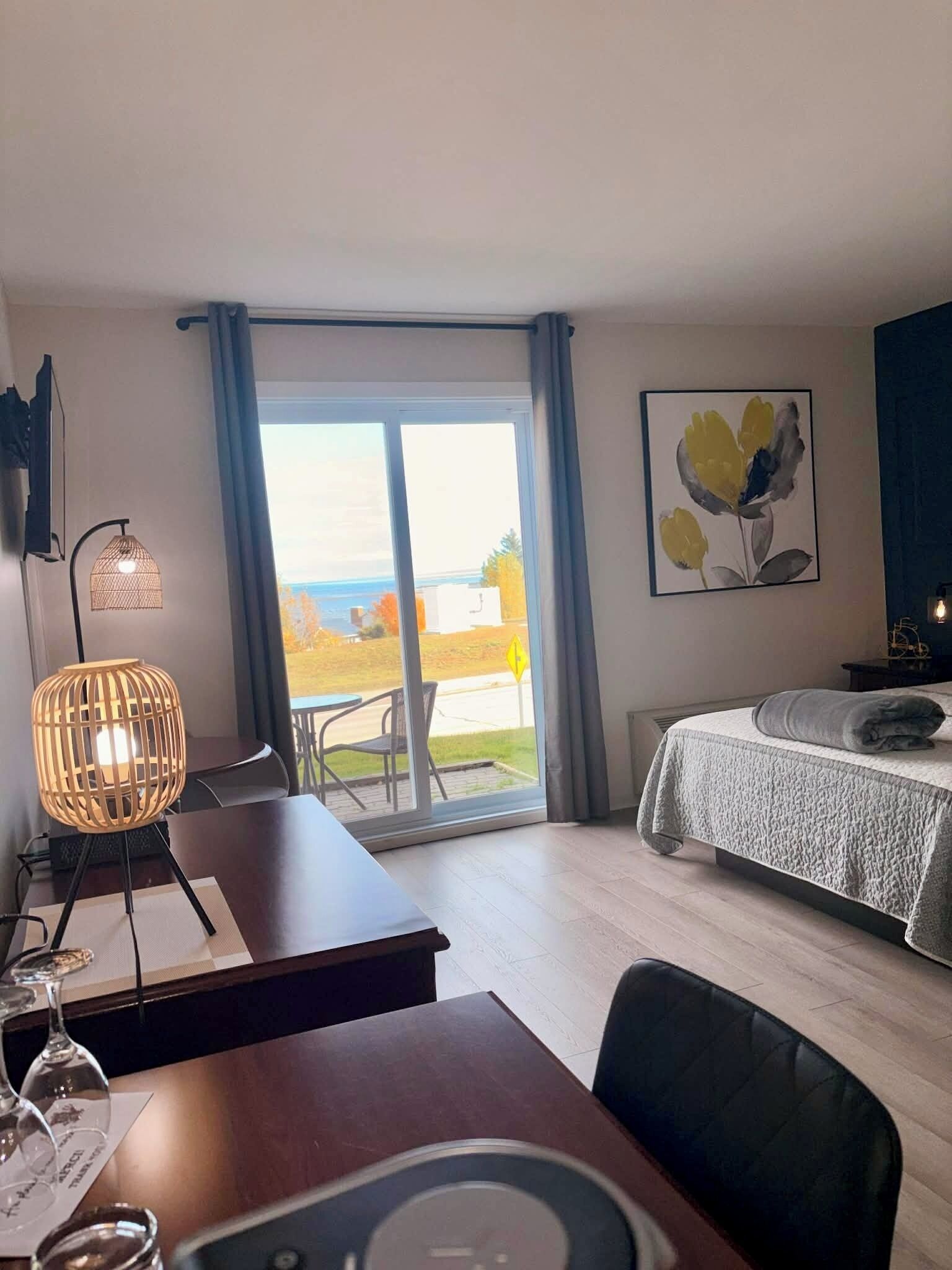 A hotel room with a bed, a desk with a lamp, a chair, and a view of the outdoors.