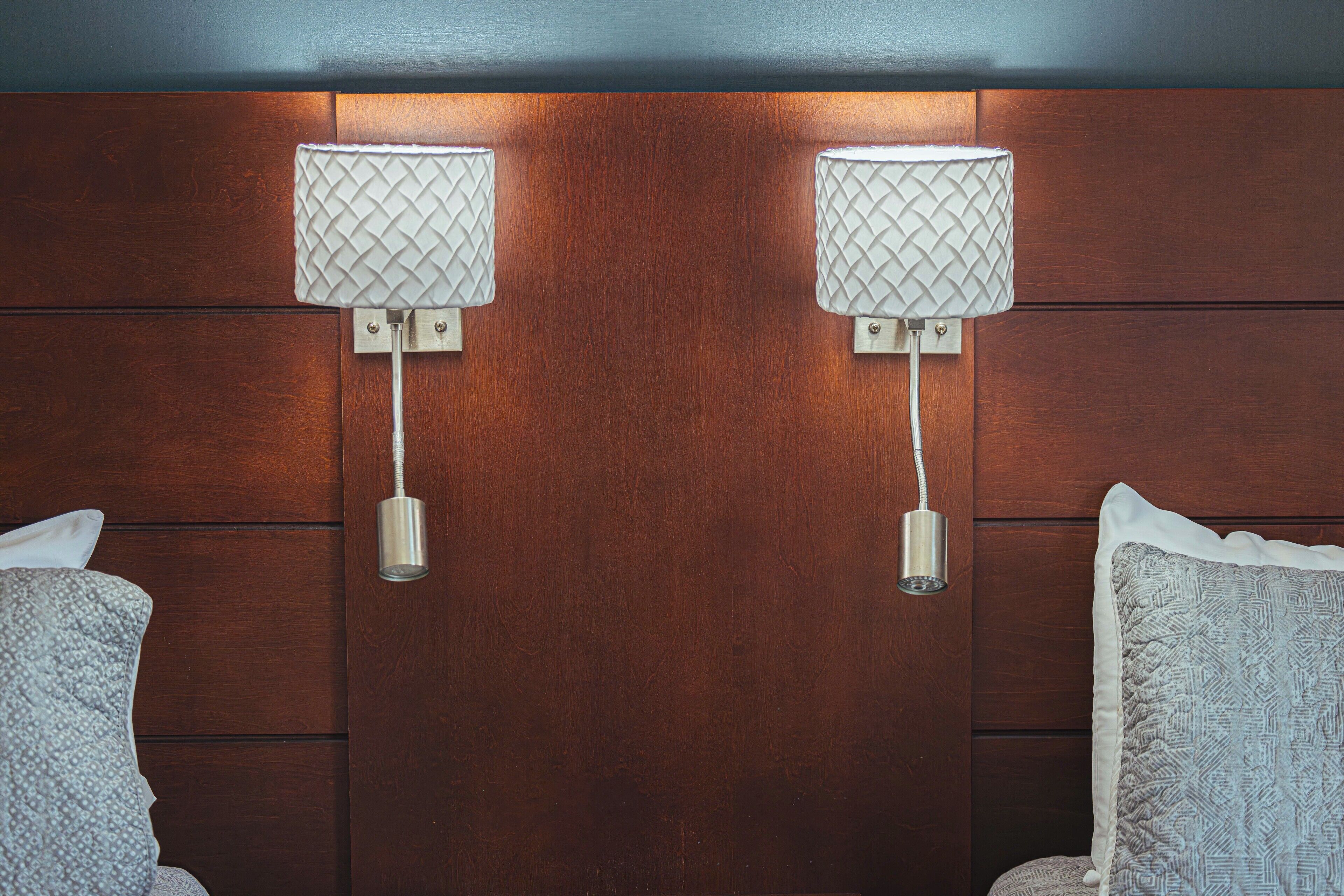 A hotel room with wooden panel walls, two bedside lamps, and two pillows.