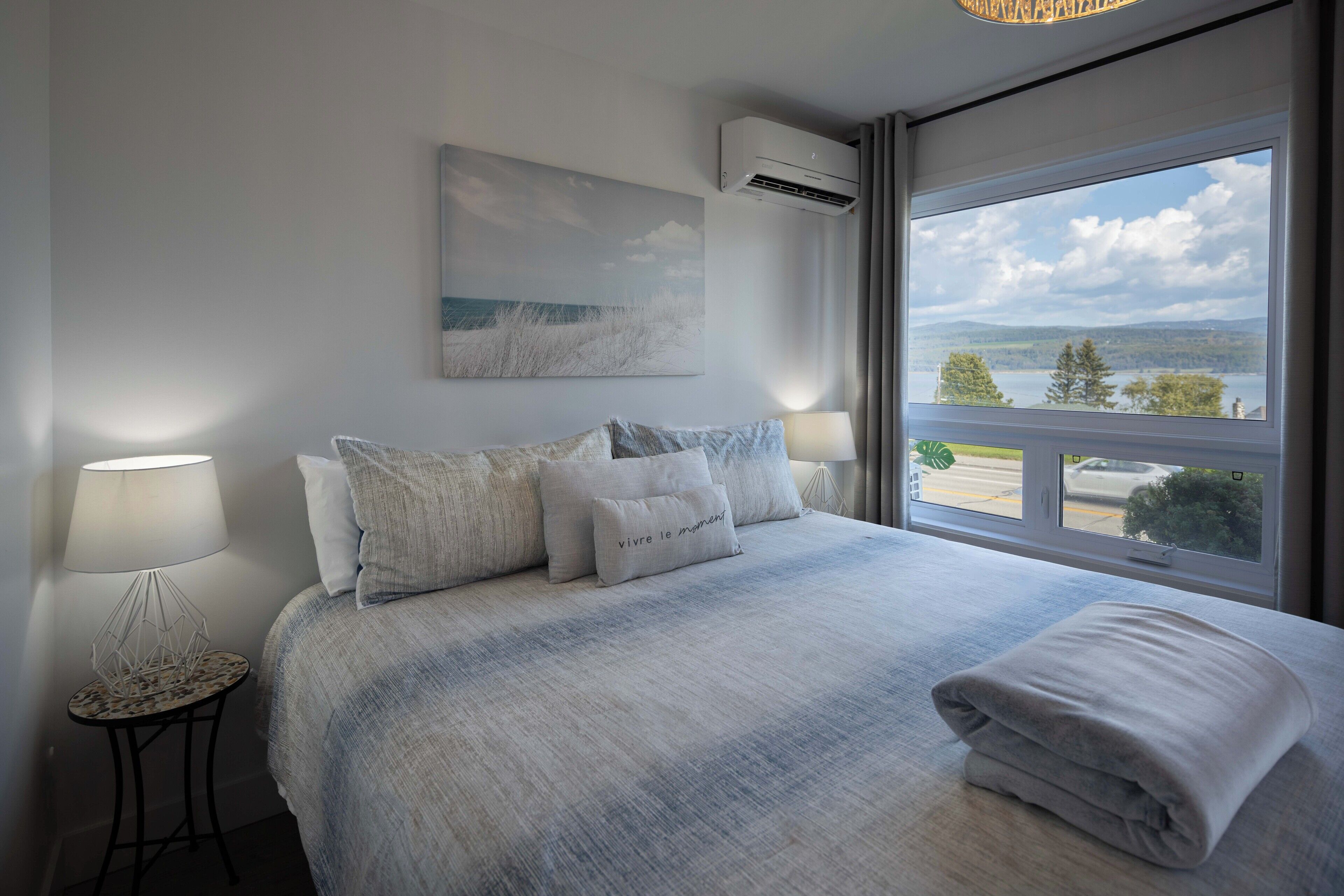 A bedroom with a large bed, a view of the outdoors, and an air conditioning unit.