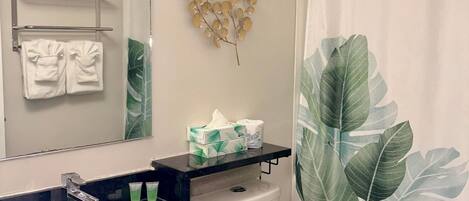Une salle de bain avec un lavabo noir, des toilettes blanches et un rideau de douche orné d’un motif de feuilles.