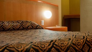 Una cama con ropa de cama estampada, una mesita de noche con un vaso y una lámpara fijada a la pared.