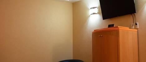 A hotel room with a bed, a wooden wardrobe, a black chair, and a mounted TV.