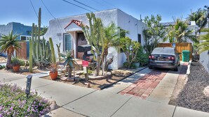 Ein Wohnhaus mit befestigter Auffahrt, einem Auto auf der Auffahrt und verschiedenen Kakteen und Pflanzen im Garten.