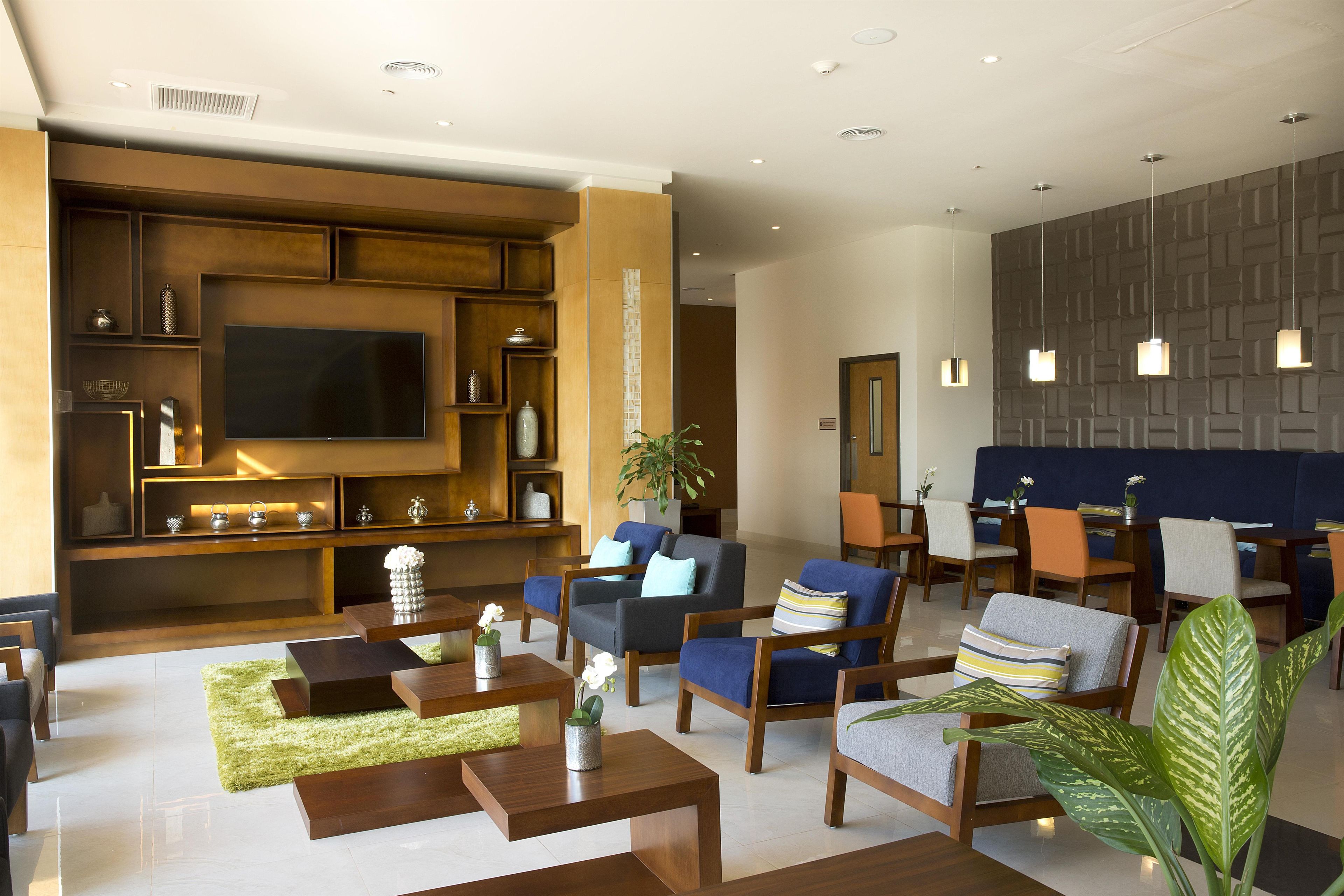 A modern living room with a flat-screen TV, wooden shelving, comfortable seating, and pendant lighting.