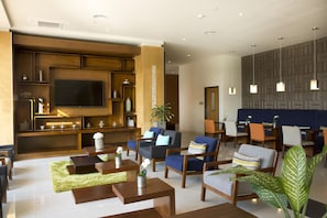 A modern living room with a flat-screen TV, wooden shelving, comfortable seating, and pendant lighting. - Hampton Inn & Suites by Hilton Paraiso (Paraiso)