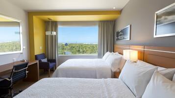 Habitación de hotel con dos camas, un escritorio, una silla, vistas al exterior y un cuadro en la pared.