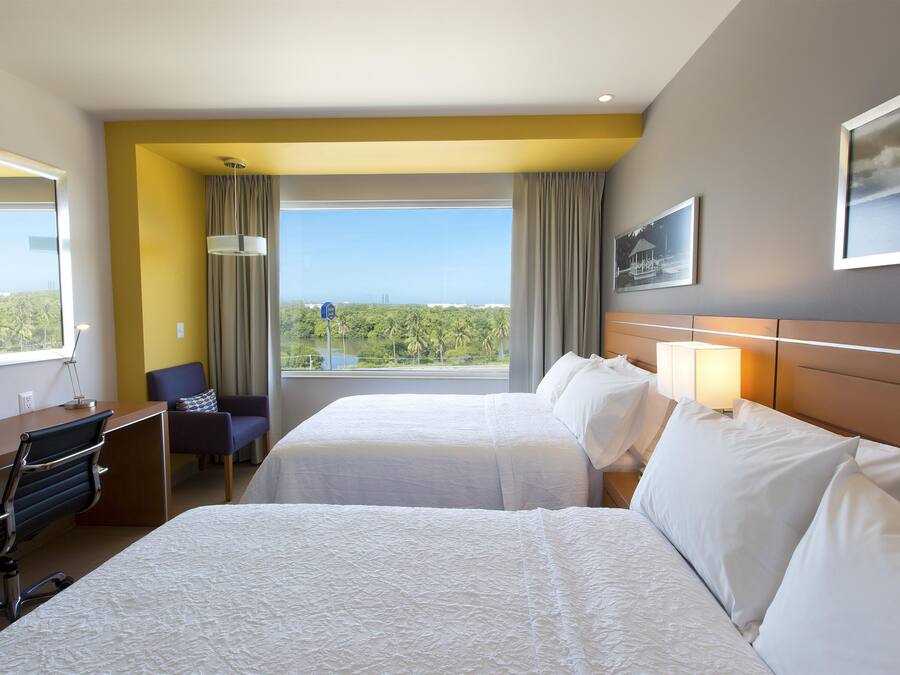 Habitación de hotel con dos camas, un escritorio, una silla, vistas al exterior y un cuadro en la pared.