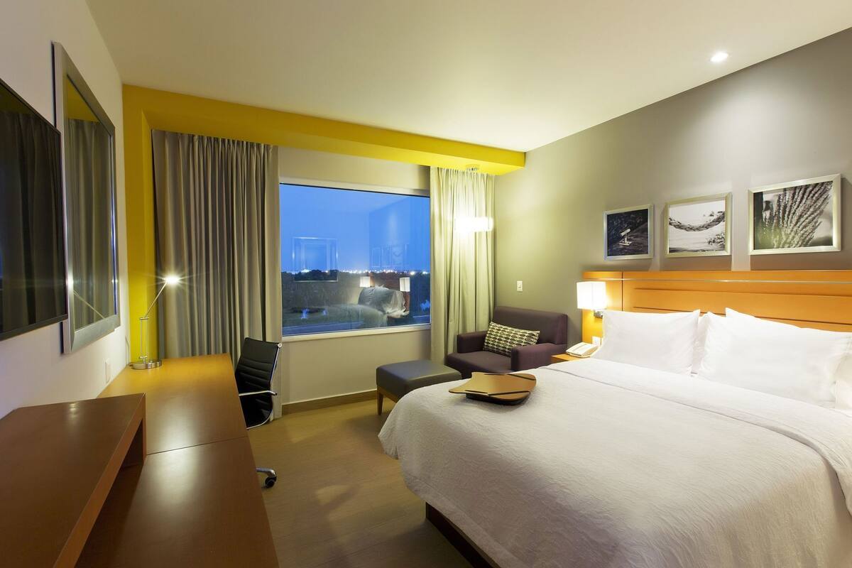 A hotel room with a bed, a desk, a chair, a window with curtains, and a city view.