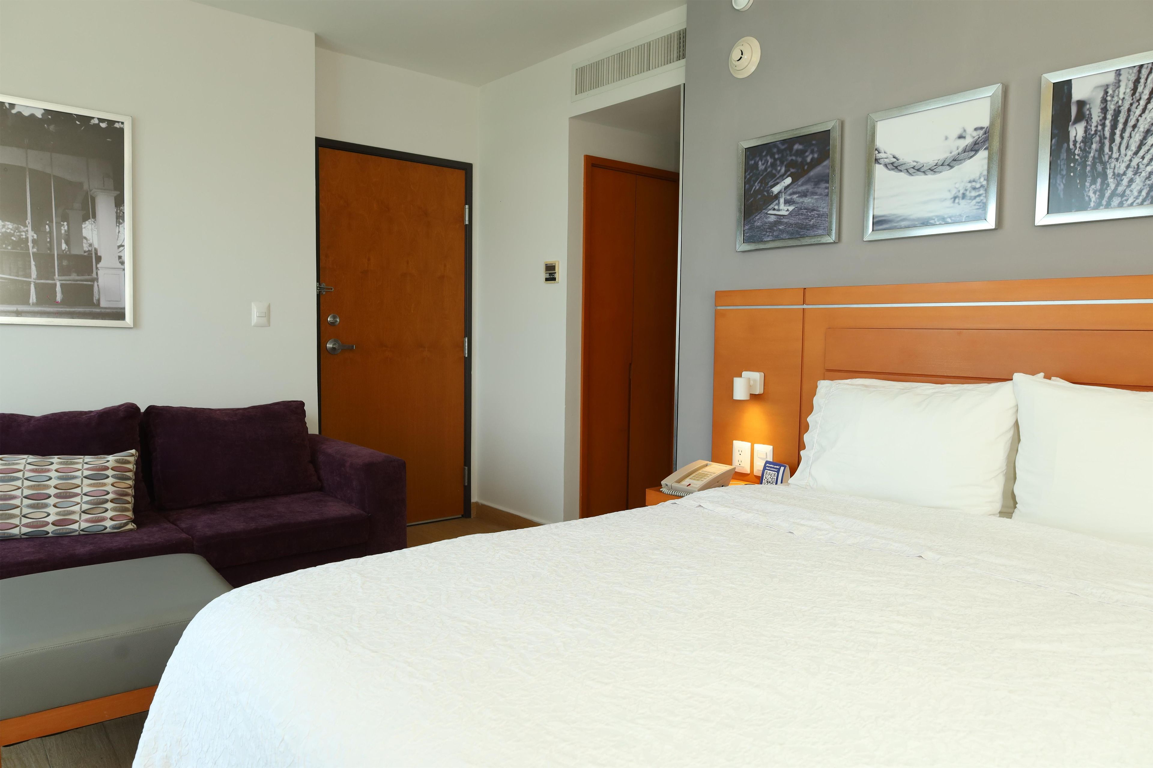Une chambre d’hôtel avec un lit, un canapé, une table de chevet avec un téléphone et une porte.