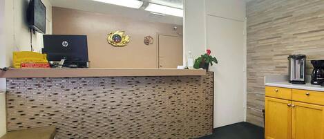A reception area with a flat-screen TV, a clock, a plant, and a coffee maker.