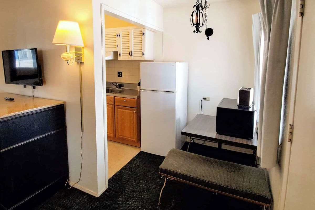 Una habitación de hotel compacta con kitchenette, televisión, escritorio con silla y una banca.
