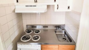 Una cocina pequeña con estufa, lavamanos y armarios blancos.