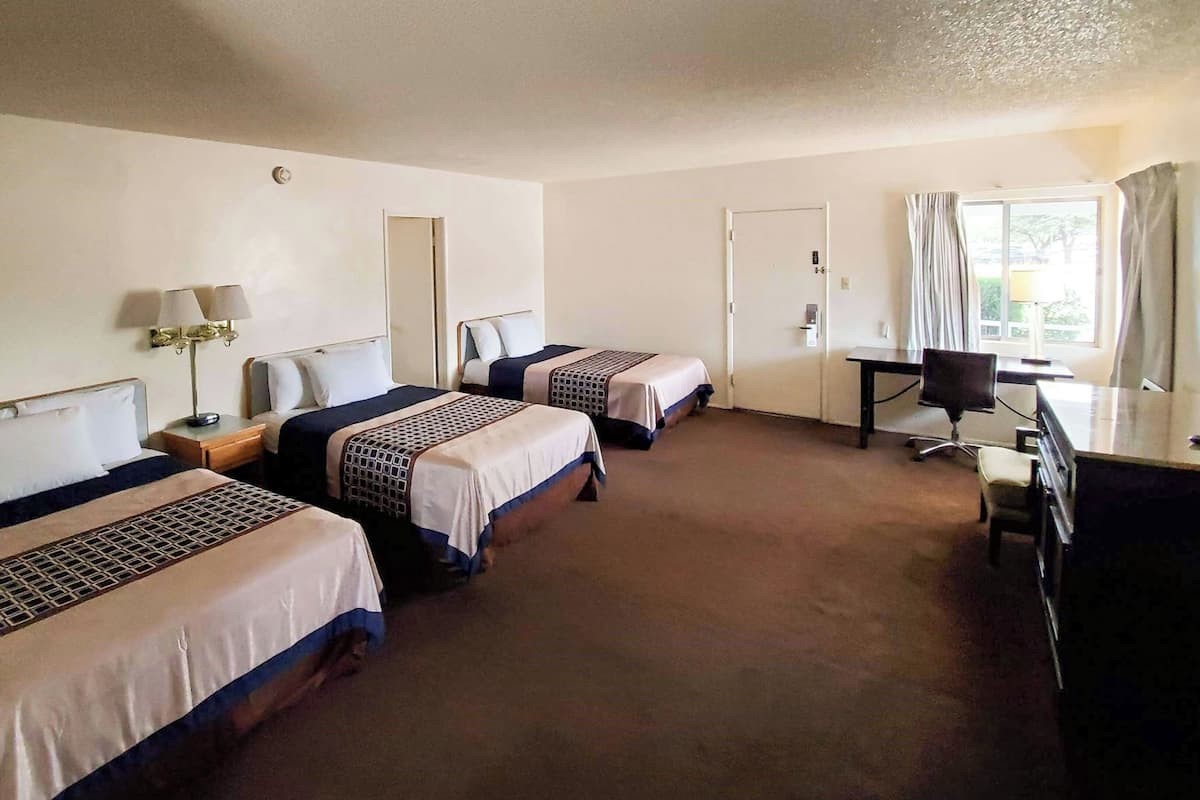 Una habitación de hotel con dos camas, un escritorio, una silla, una lámpara y una ventana con cortinas.