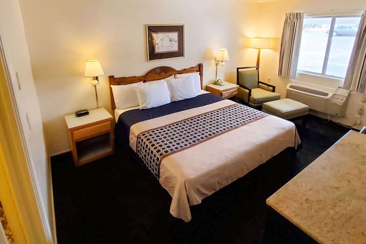 Habitación de hotel con cama, dos mesitas de noche, escritorio, silla, ventana con cortinas y un cuadro en la pared.