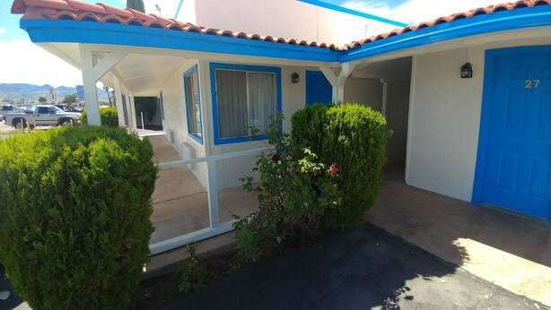 Un edificio con puerta azul que indica el número 27, un porche cubierto y un pequeño jardín.