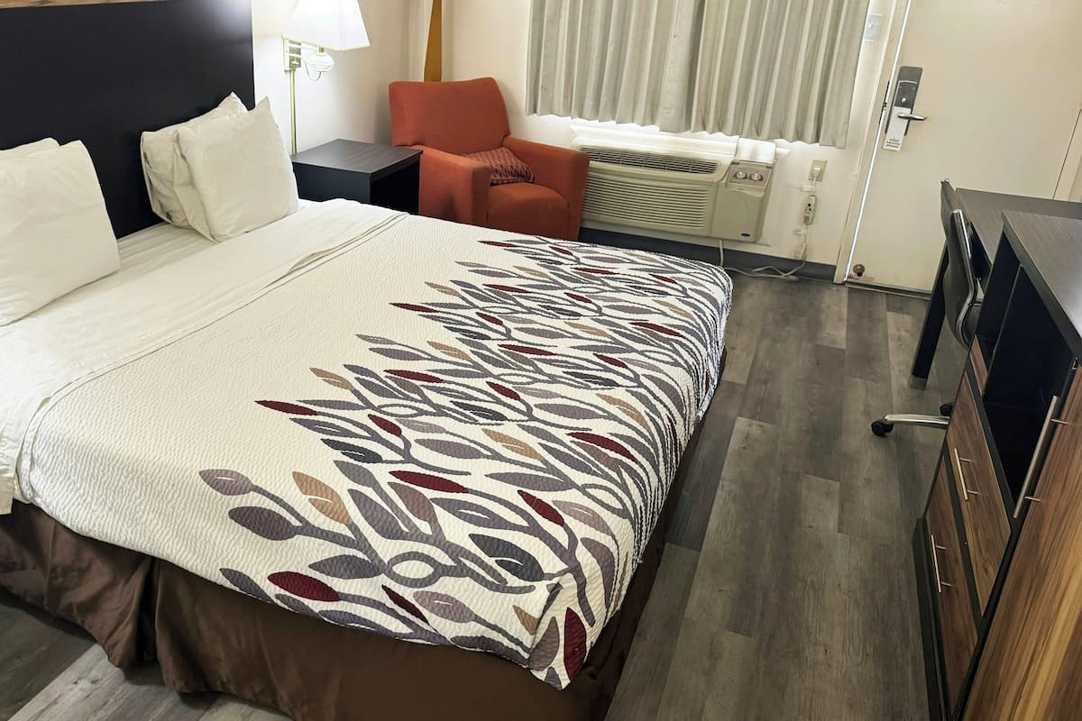 Una habitación de hotel con una cama, una silla, un escritorio y un equipo de aire acondicionado.