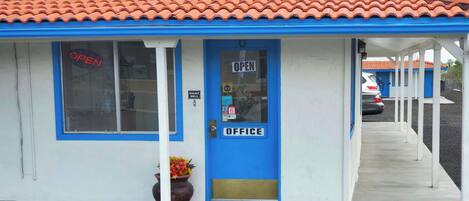 Un edificio azul y blanco con techo de tejas rojas, una puerta azul con un letrero que dice 'ABIERTO', un letrero que dice 'TIMBRE DE NOCHE' y un letrero de 'VISA'.
