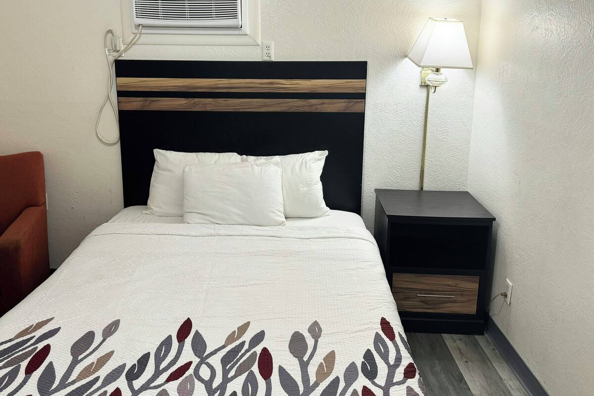Habitación de hotel ordenada con cama, mesita de noche, lámpara, sillón y un calentador de pared.