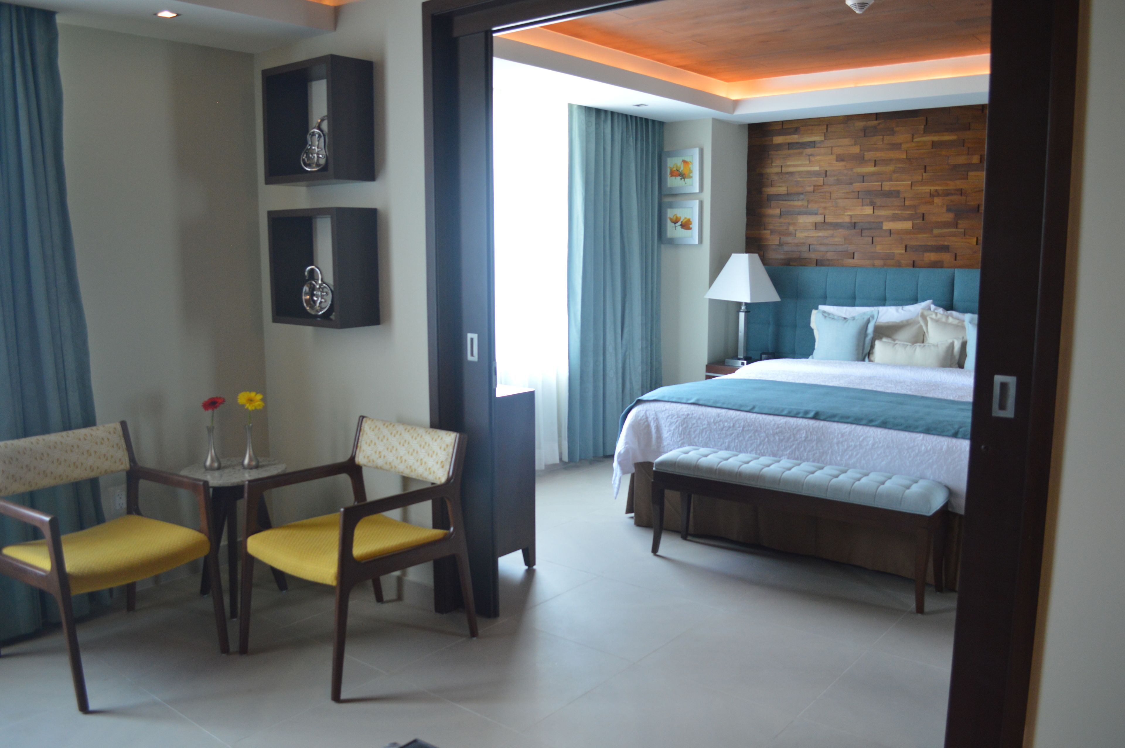 Una habitación de hotel con cama, escritorio y dos sillas, lámpara y un cuadro en la pared.