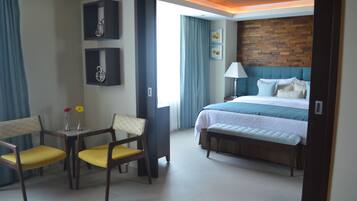 Una habitación de hotel con cama, escritorio y dos sillas, lámpara y un cuadro en la pared.