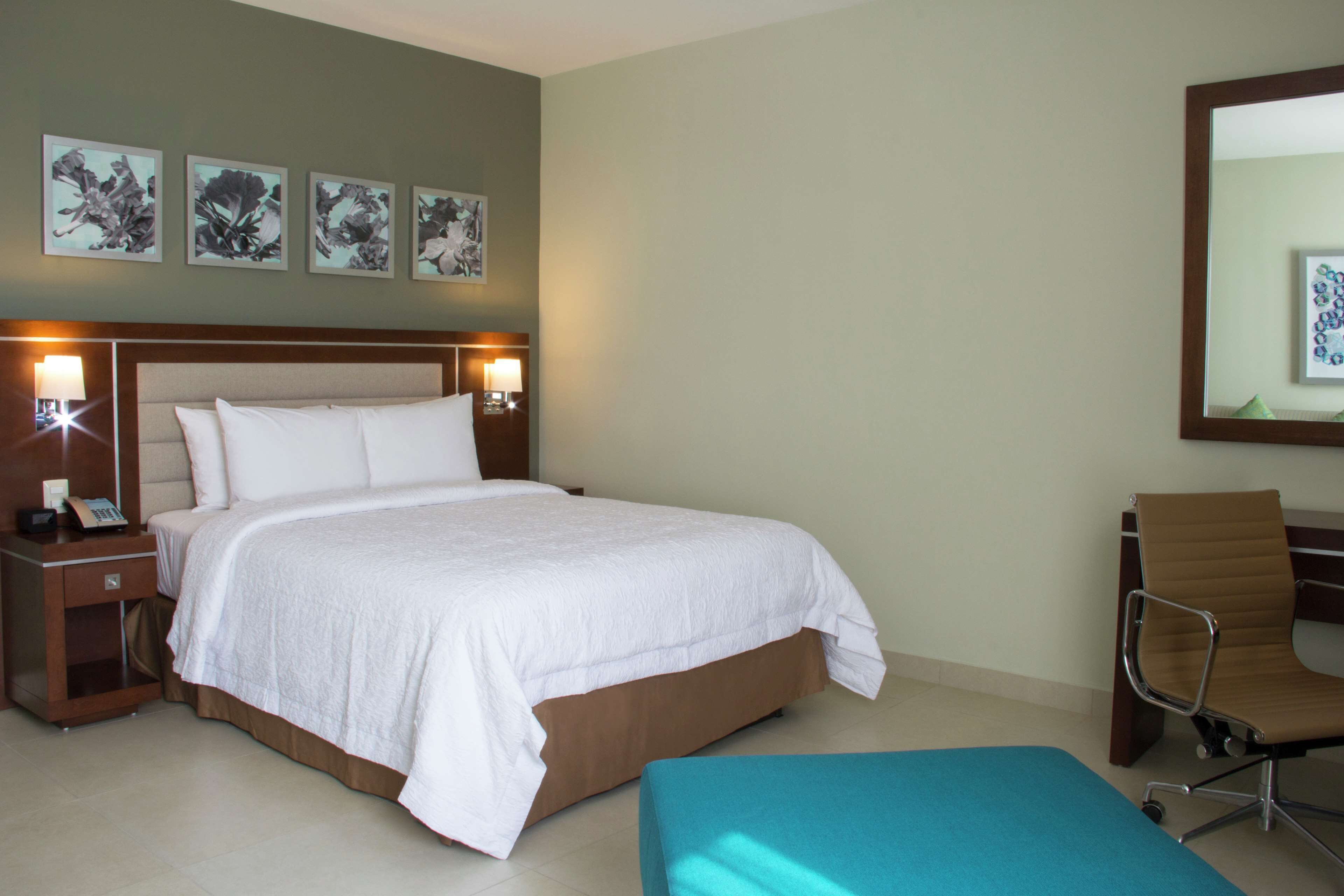 A hotel room with a large bed, a bedside table with a lamp, a chair, and artwork on the wall.