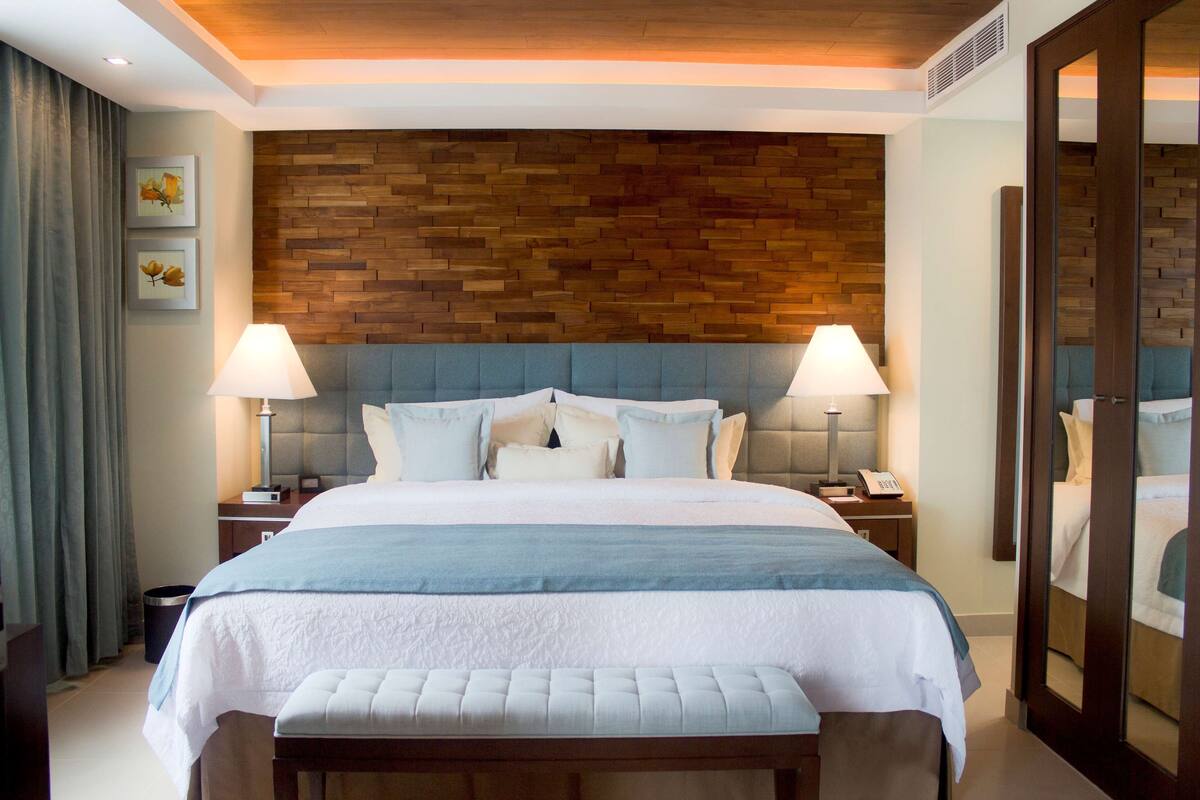 Une chambre d’hôtel avec un grand lit, deux tables de chevet, une tête de lit en bois et un miroir.