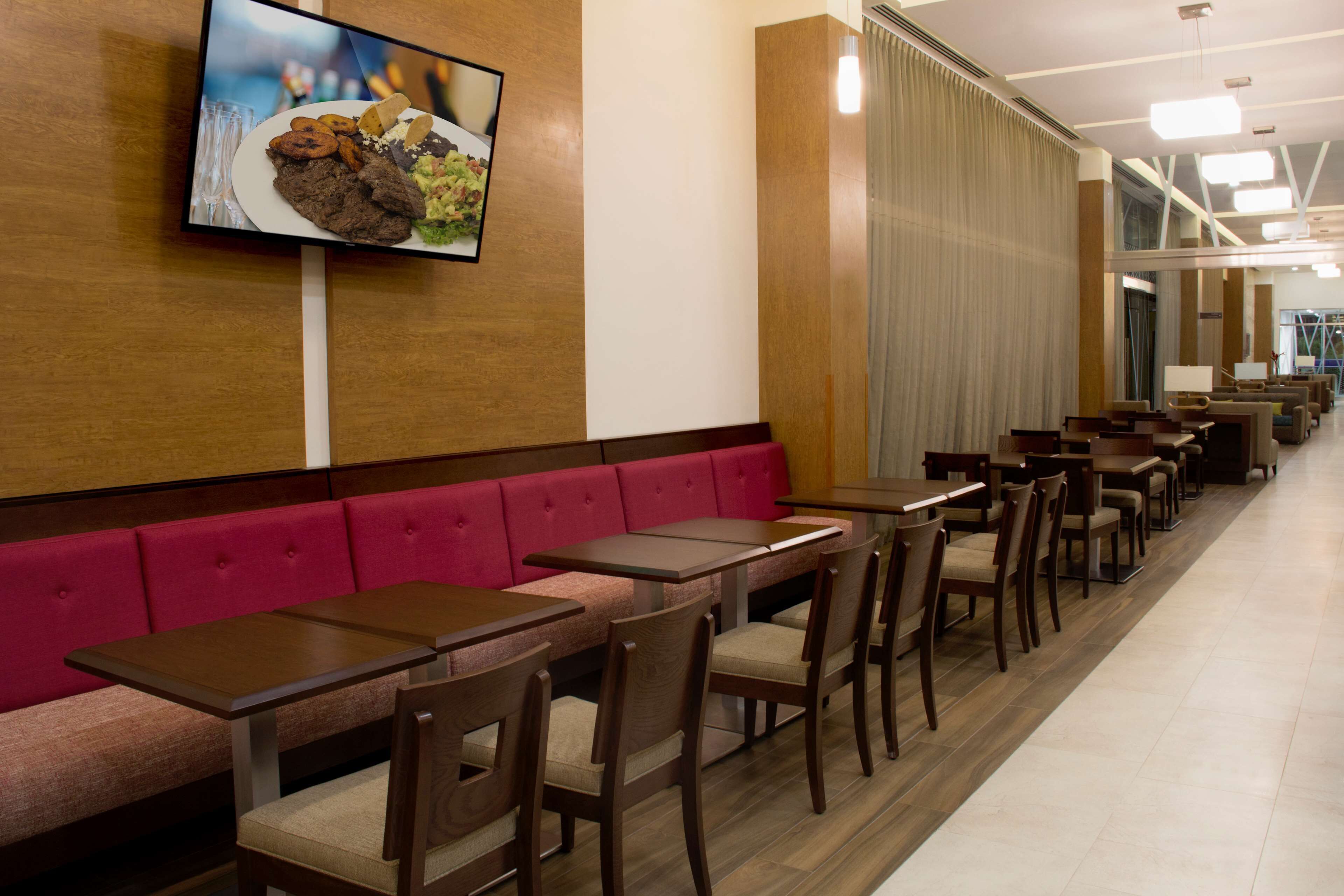 Un restaurante con cabinas y mesas, un televisor mostrando comida, y una barra larga con sillas.