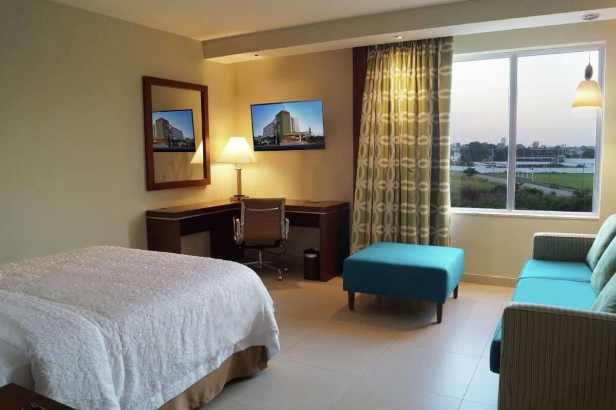 Une chambre d’hôtel avec un lit, un bureau, une chaise et une vue sur la ville.