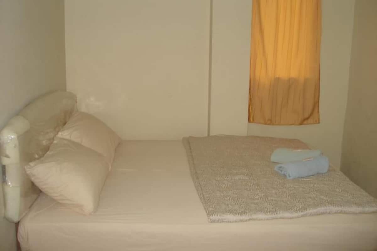 Un letto singolo con materasso e cuscini bianchi, una coperta beige e un asciugamano blu.