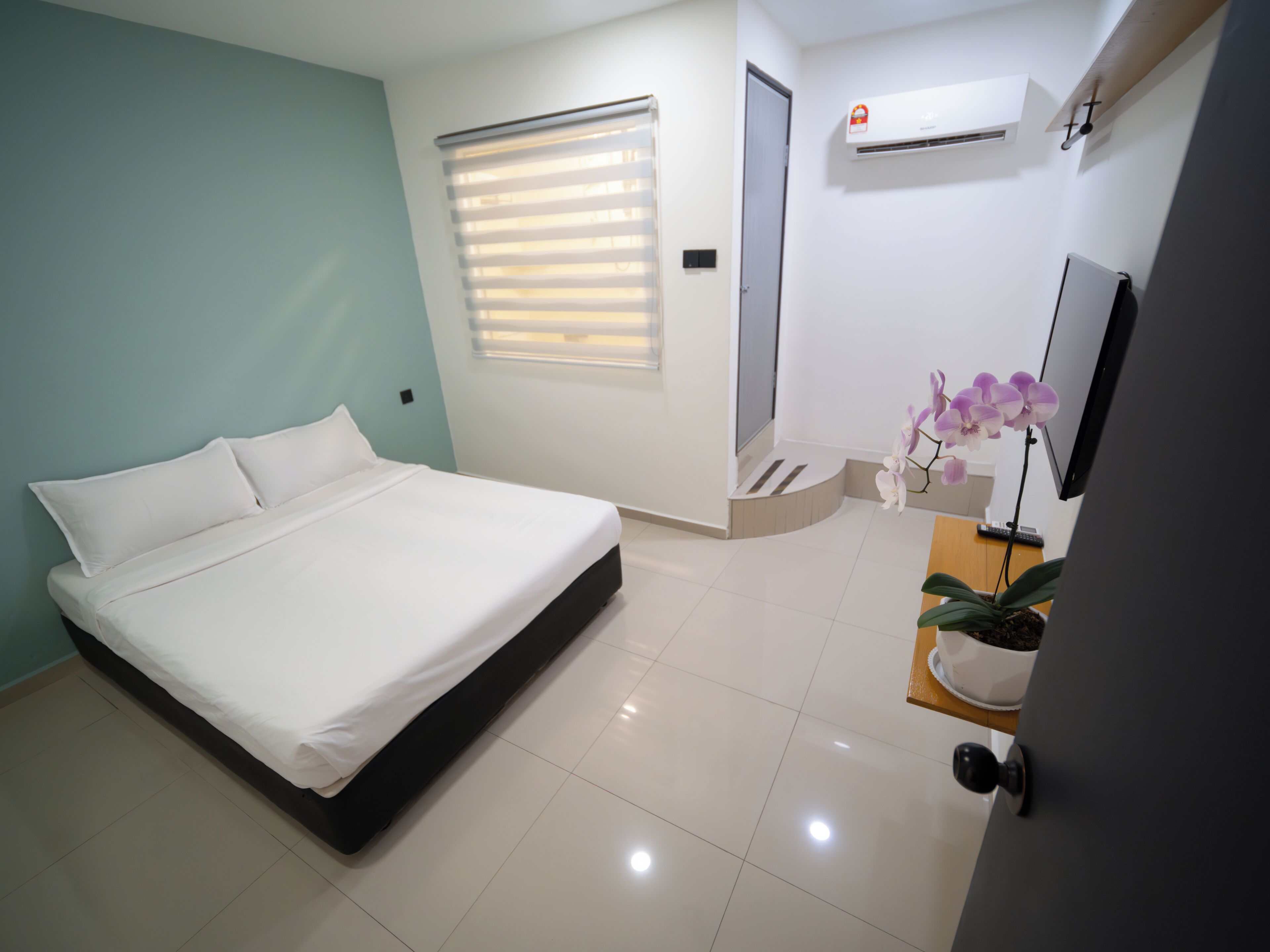A modern bedroom with a bed, a window with blinds, an air conditioning unit, and a small potted orchid.