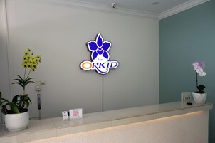 A reception desk with a neon sign for 'Orkid Inn' and potted plants on either side.