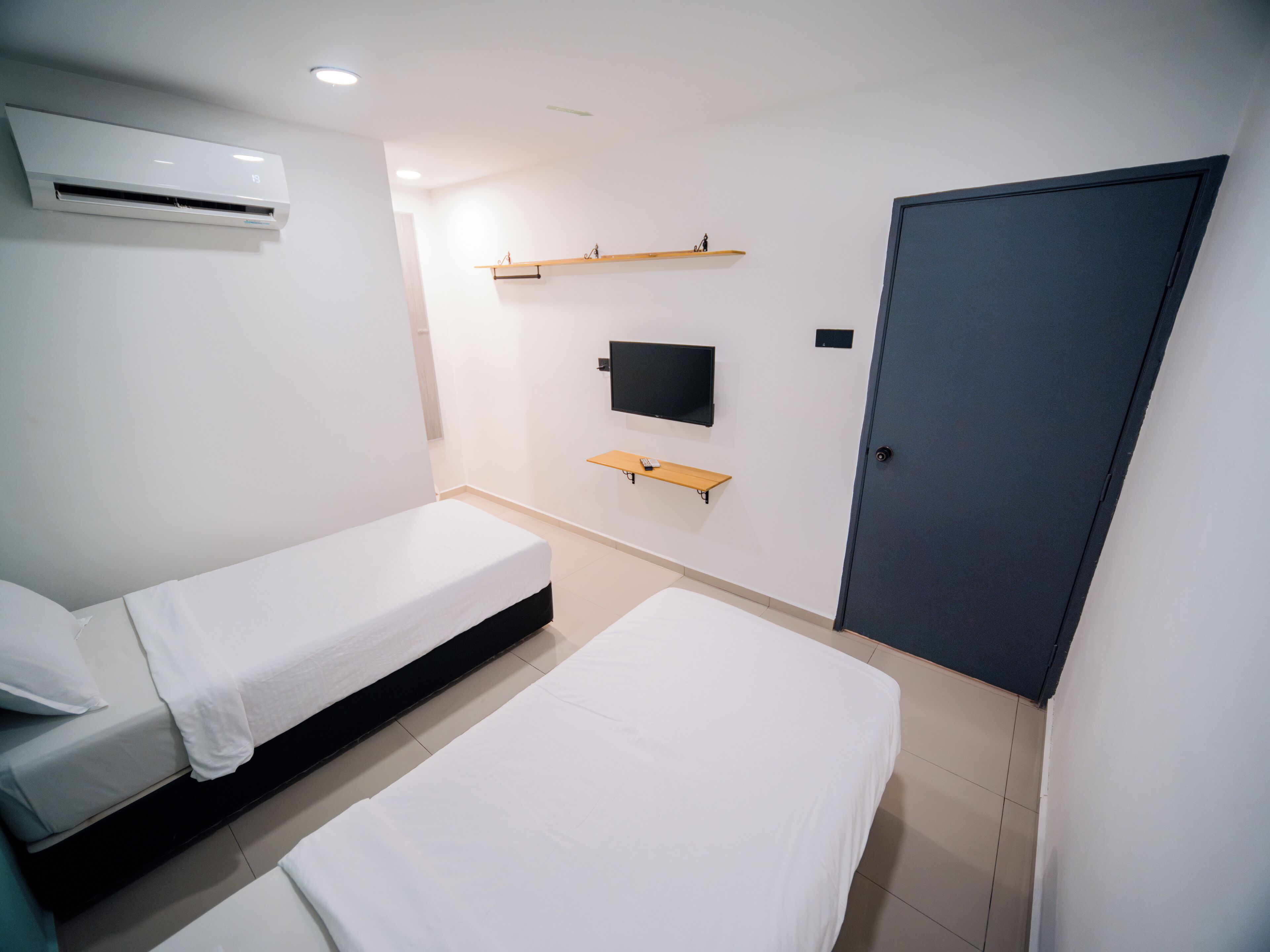 A modern hotel room with two single beds, a flat-screen TV mounted on the wall, and a wardrobe.