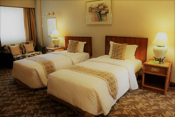 A hotel room with two beds, a sofa, a lamp, and a painting on the wall.