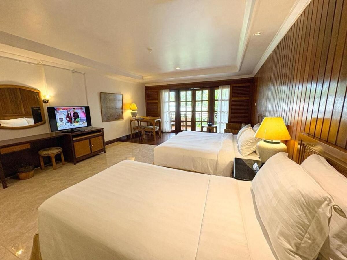A hotel room with two beds, a TV, a desk with a chair, and a window with blinds.