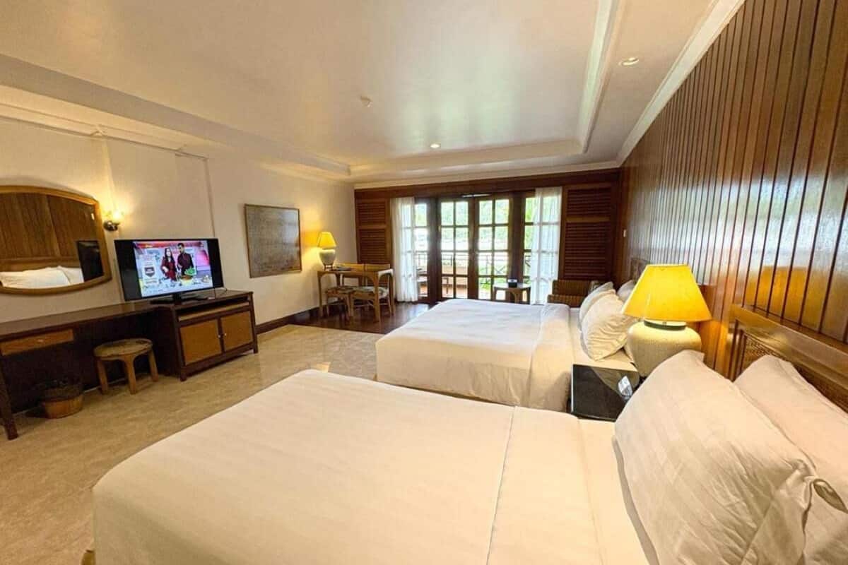 A hotel room with two beds, a TV, a desk with a chair, and a window with blinds.