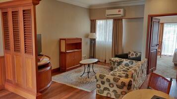 A hotel room with a wooden cabinet, a sofa, a small table, and a ceiling fan.