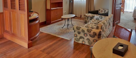 A hotel room with a wooden cabinet, a sofa, a small table, and a ceiling fan.