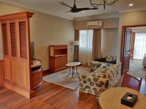 A hotel room with a wooden cabinet, a sofa, a small table, and a ceiling fan.
