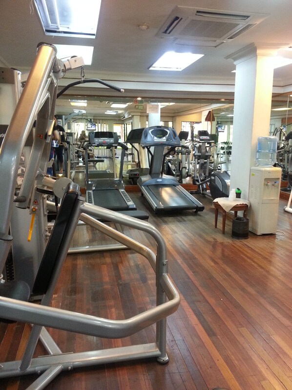 A gym with various exercise machines, wooden flooring, and a water dispenser. - Tiara Labuan Hotel (Labuan)