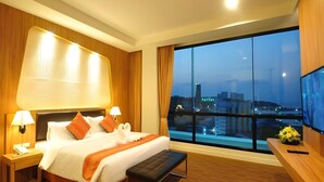 A hotel room with a large bed, bedside lamps, a wooden floor, a large window with a city view, and a TV on the wall. - VC. Pattaya (Pattaya)