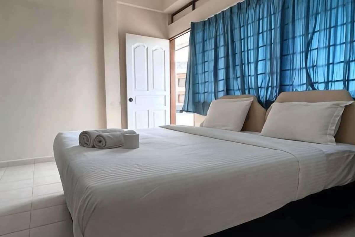 A hotel room with a bed, a door, and a window with blue curtains.