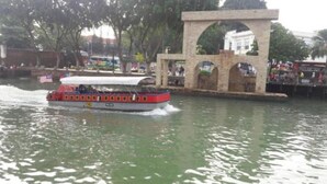 Una barca con decorazioni rosso e bianco che naviga in un corso d'acqua, passando accanto a una struttura in pietra con archi.