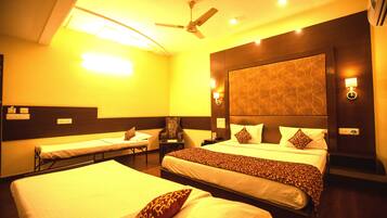 A hotel room with two single beds, a double bed, a ceiling fan, bedside lamps, and a patterned headboard.