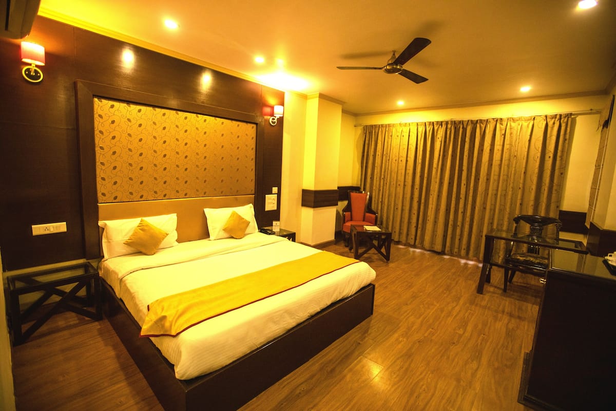 A hotel room with a large bed, a desk, a chair, a ceiling fan, and a window with curtains.
