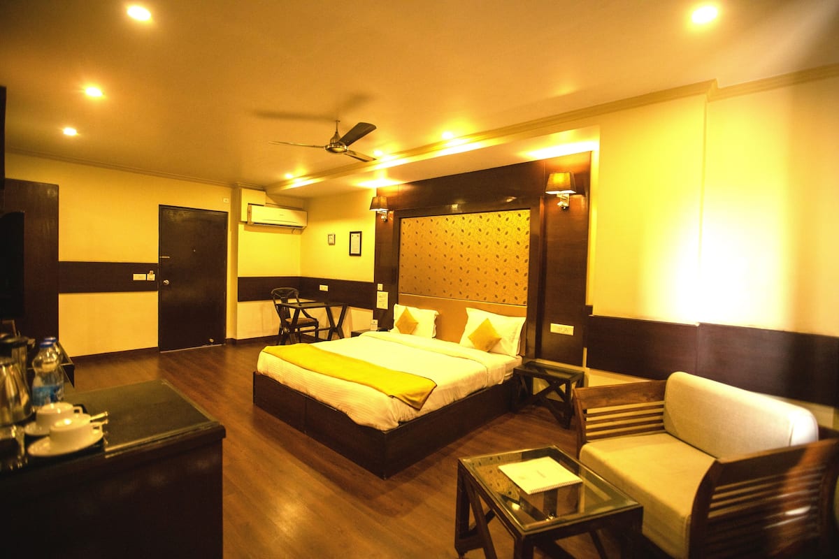 A hotel room with a large bed, a sofa, a small table, a desk, and a ceiling fan.