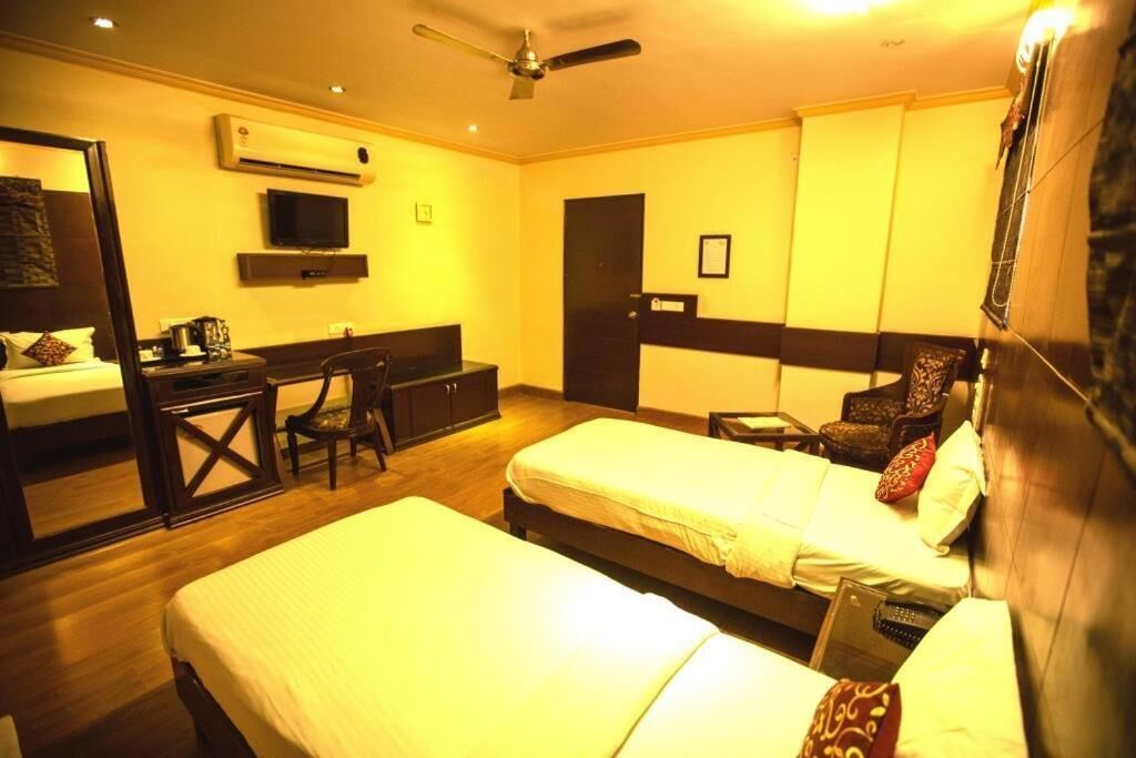 A hotel room with two beds, a desk, a chair, a television, and an air conditioning unit.