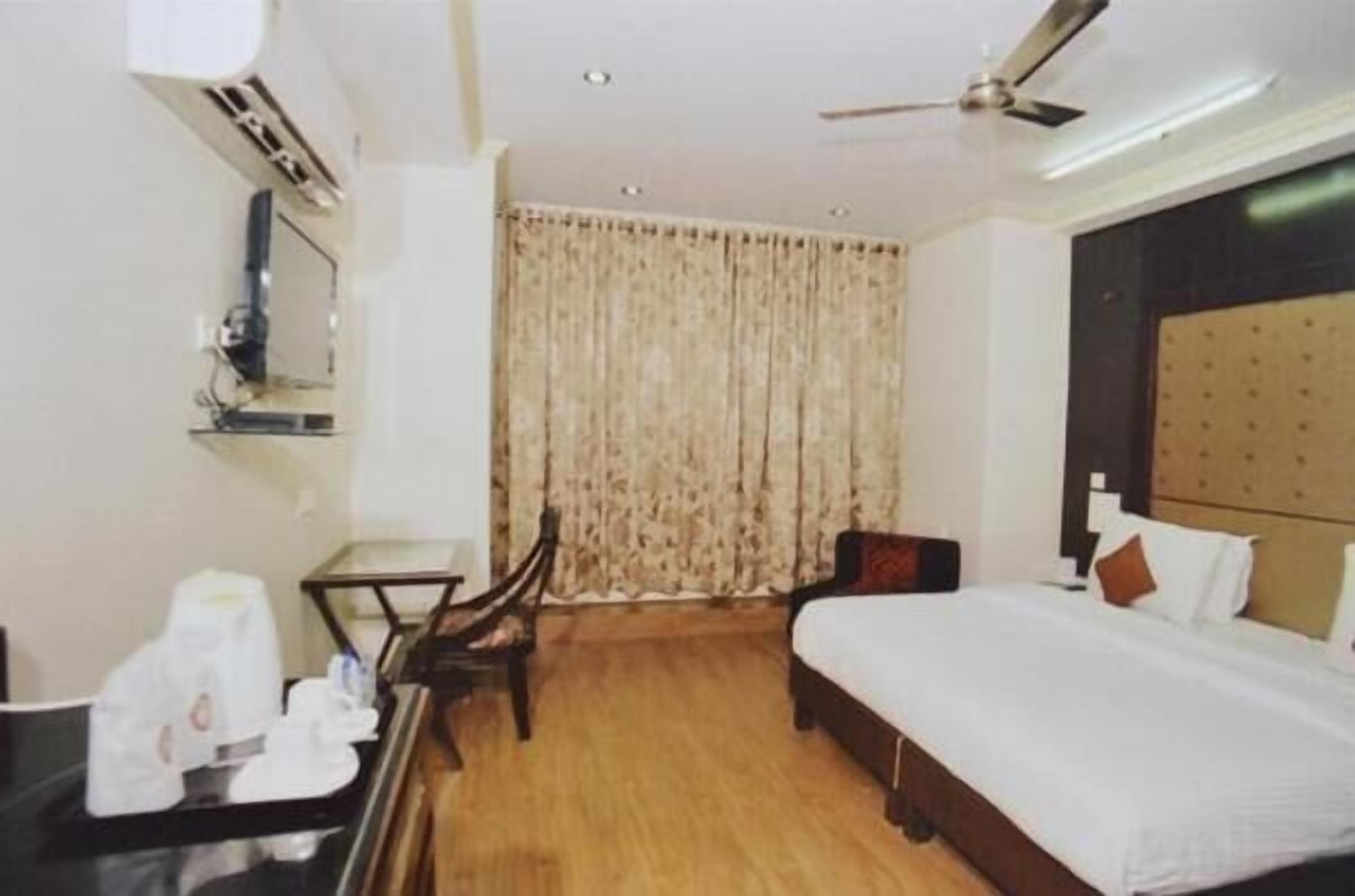 A hotel room with a bed, a desk, a chair, a ceiling fan, and a window with curtains.