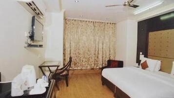 A hotel room with a bed, a desk, a chair, a ceiling fan, and a window with curtains.