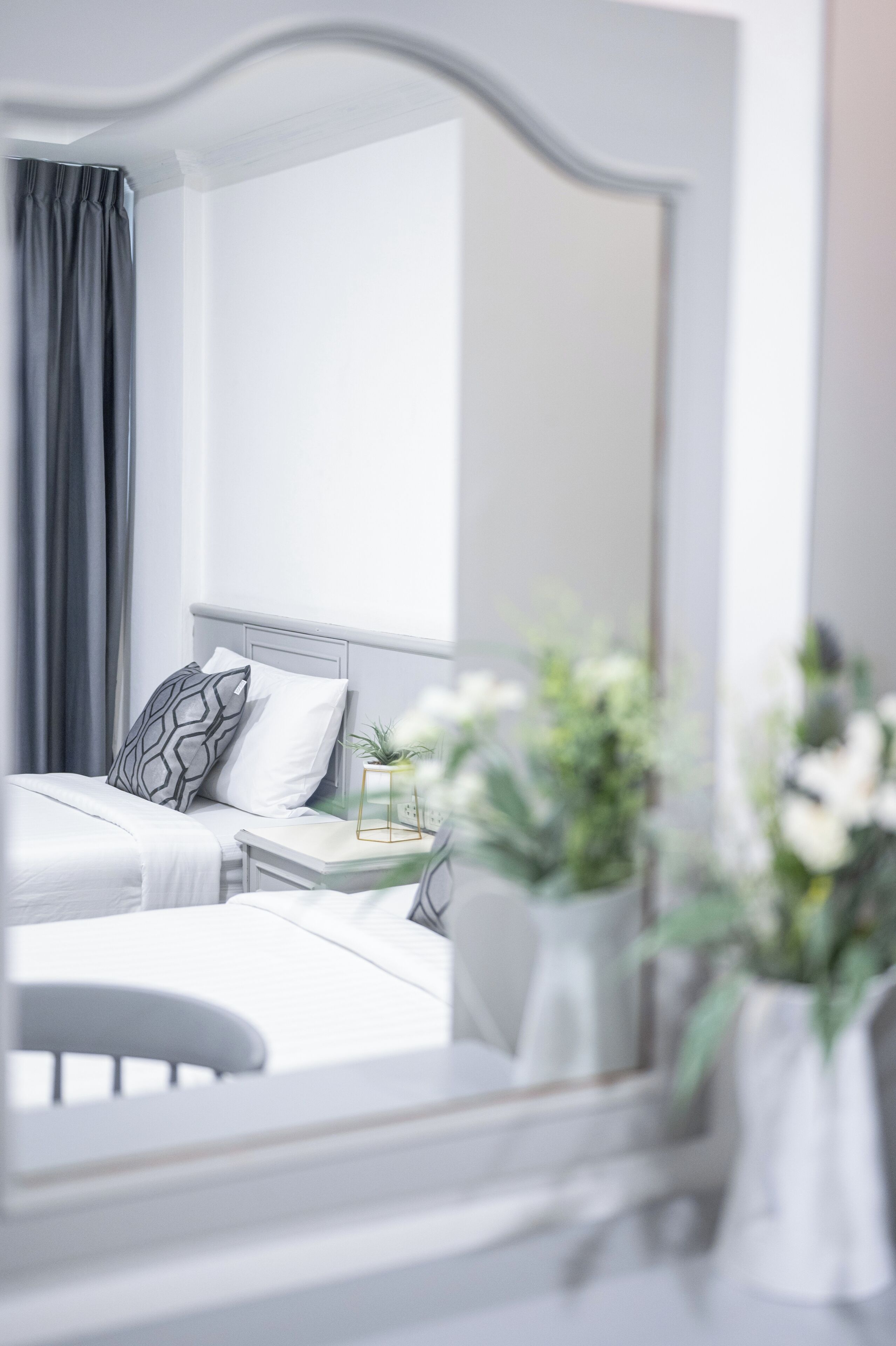 Een moderne hotelkamer met een groot bed, een nachtkastje met een lamp en een spiegel die de kamer weerspiegelt.