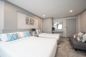 Una habitación de hotel con dos camas, un sofá gris, un escritorio pequeño y un espejo.